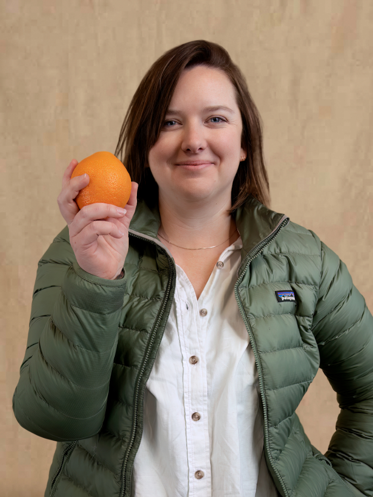 a woman in a green jacket holding an orange.