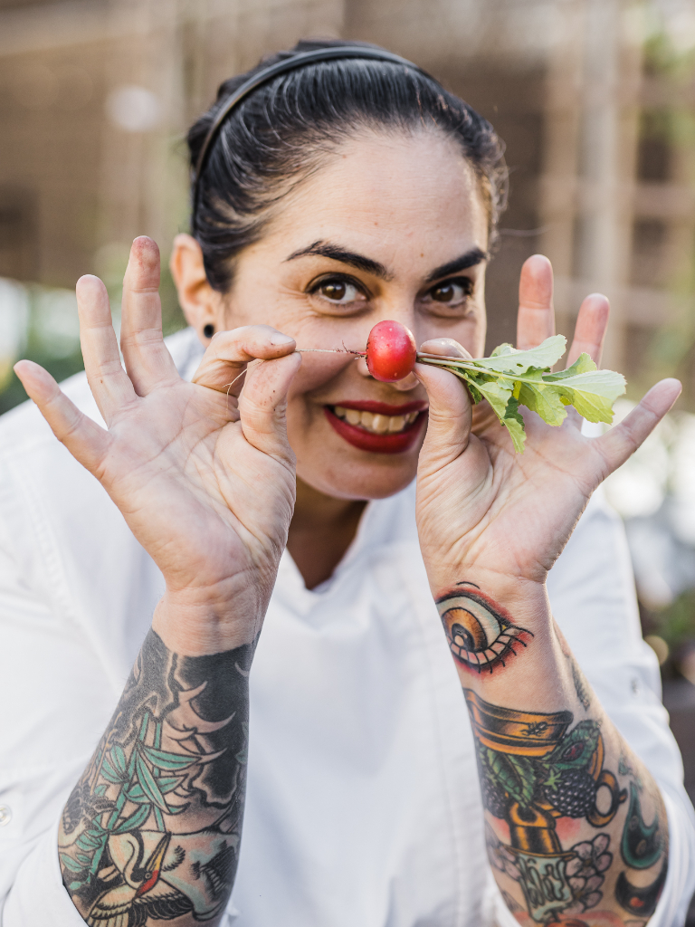 A woman wearing a chef's hat with tattoos on her face.
